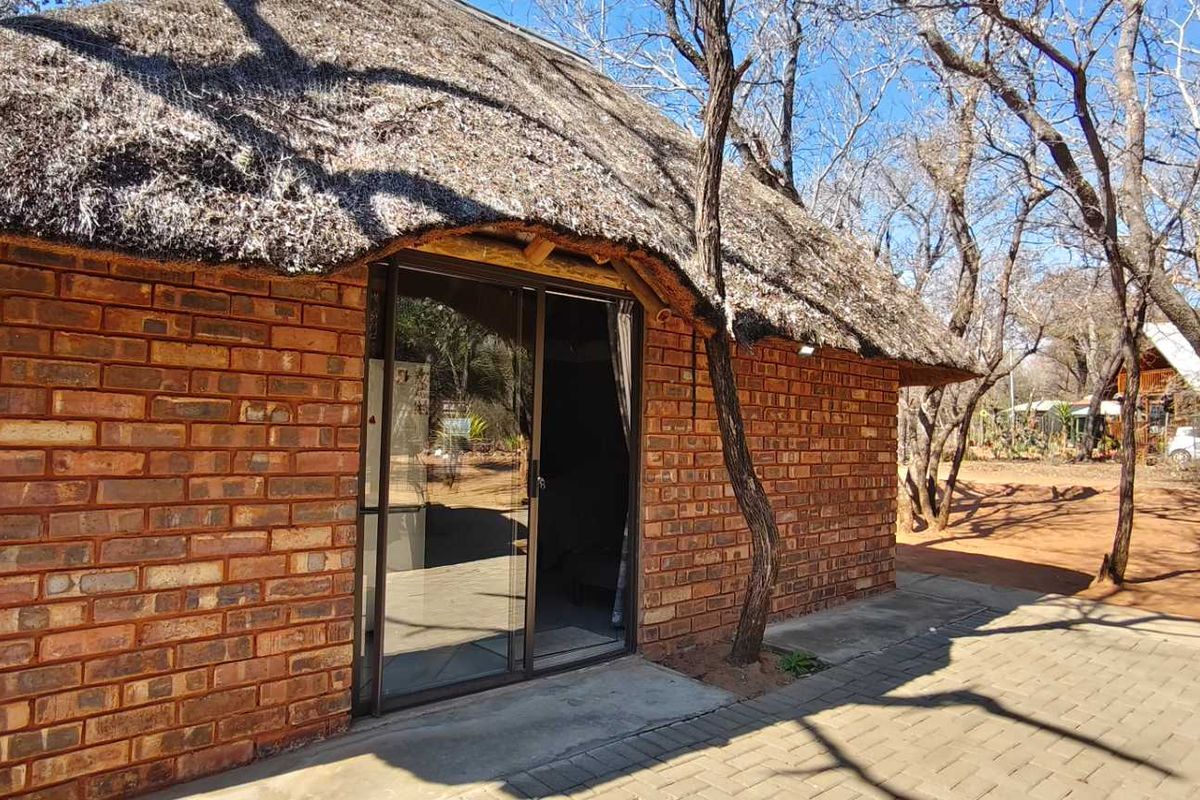 Rear view of a rustic brick house featuring a traditional thatch roof, sliding glass doors, and a paved patio area.