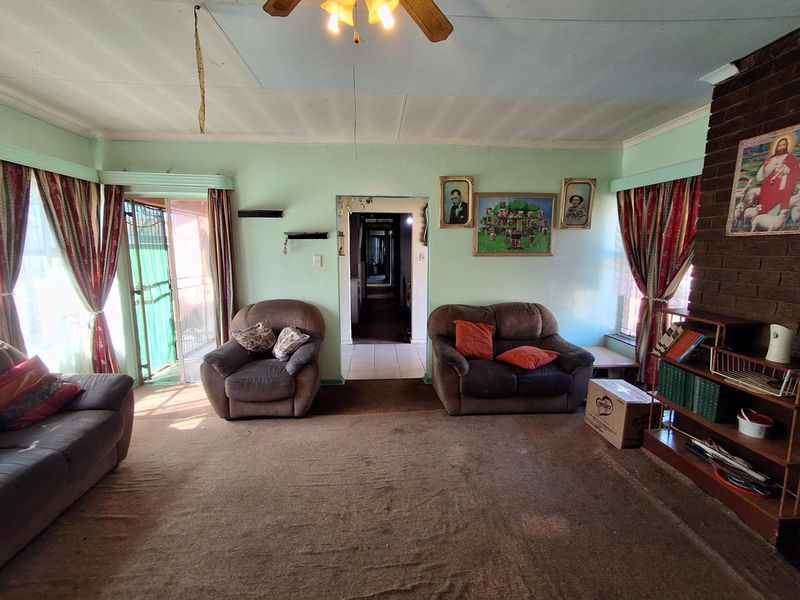 Spacious living room featuring a brick fireplace, ceiling fan, and sliding door access, requiring cosmetic updates to flooring and ceiling finishes.