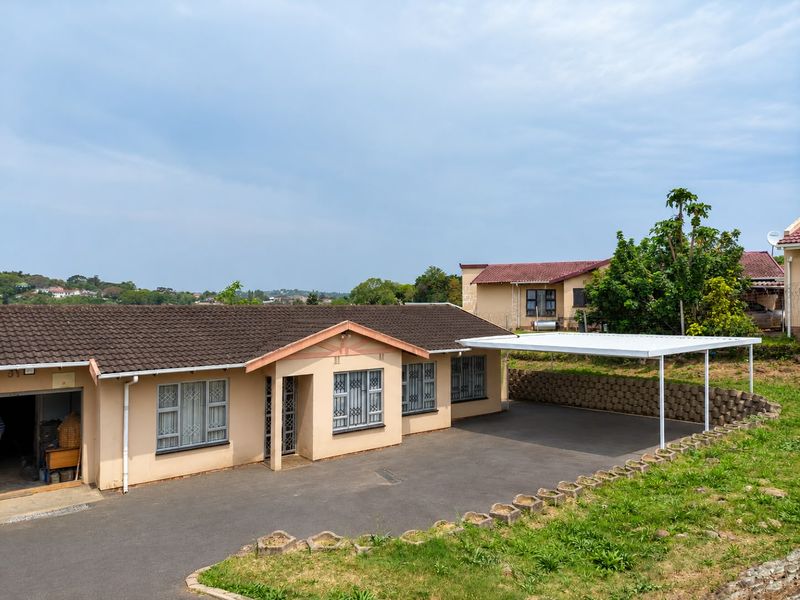 Front exterior view of a single-story house featuring a tiled roof, paved driveway, and a covered carport area.