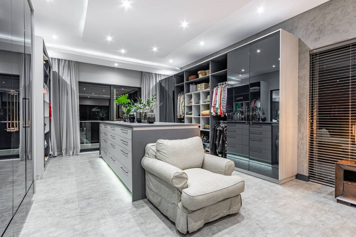 A spacious, modern walk-in closet featuring extensive built-in cabinetry, a central island with storage drawers, recessed ceiling lighting, and large glass sliding doors.