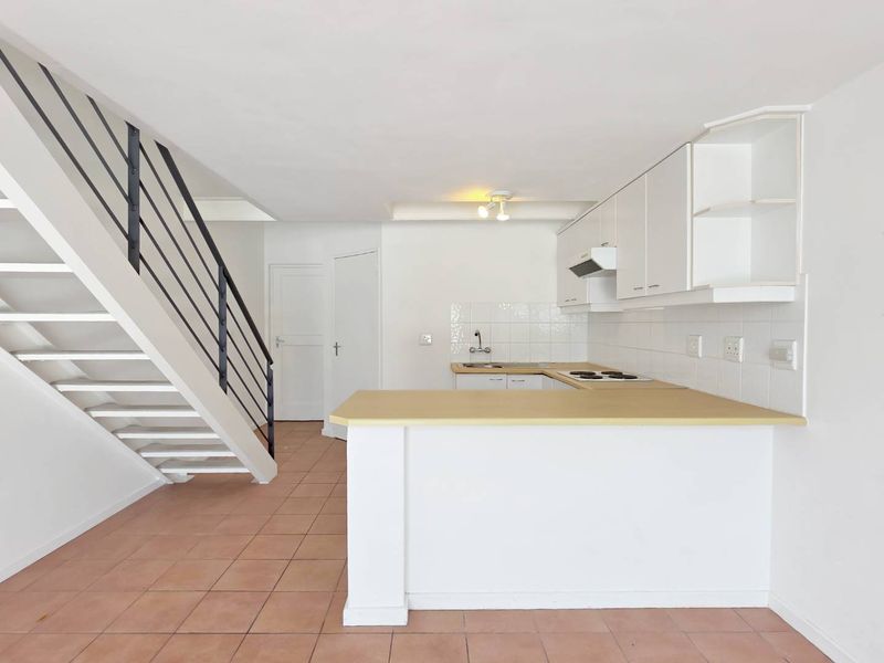Open plan kitchen and living area featuring tiled flooring, built-in cabinetry, a hob, extractor fan, and a staircase leading to the upper level.