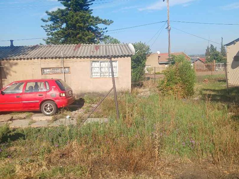 Rear exterior view of the property showing a detached structure with corrugated roofing, security bars on windows, and an expansive, unmaintained garden area.
