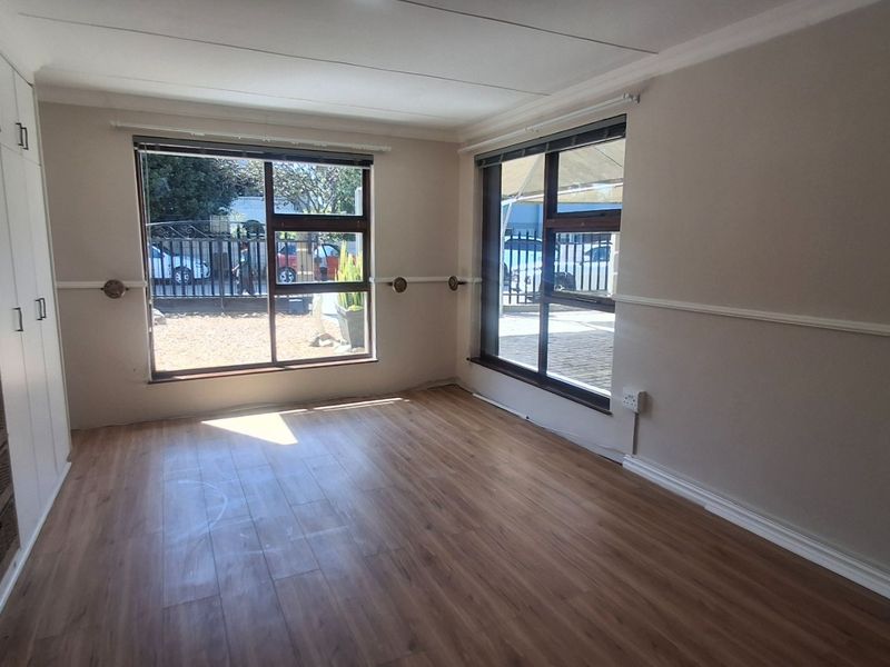 A bright, empty bedroom featuring laminate flooring, built-in cupboards, and large windows providing natural light.