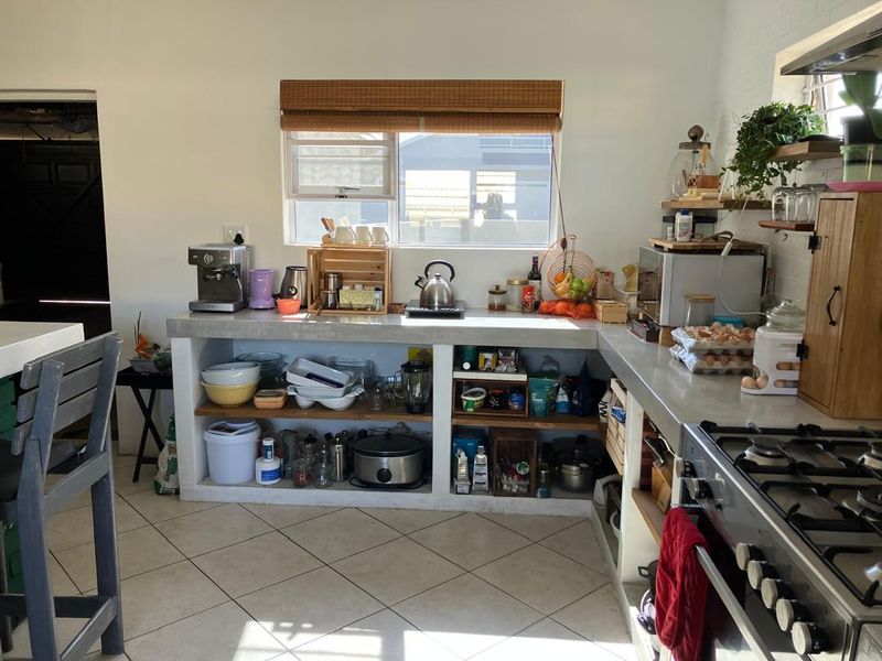 A functional kitchen featuring concrete countertops, open shelving, and a gas stove, with tiled flooring and natural light from a window.