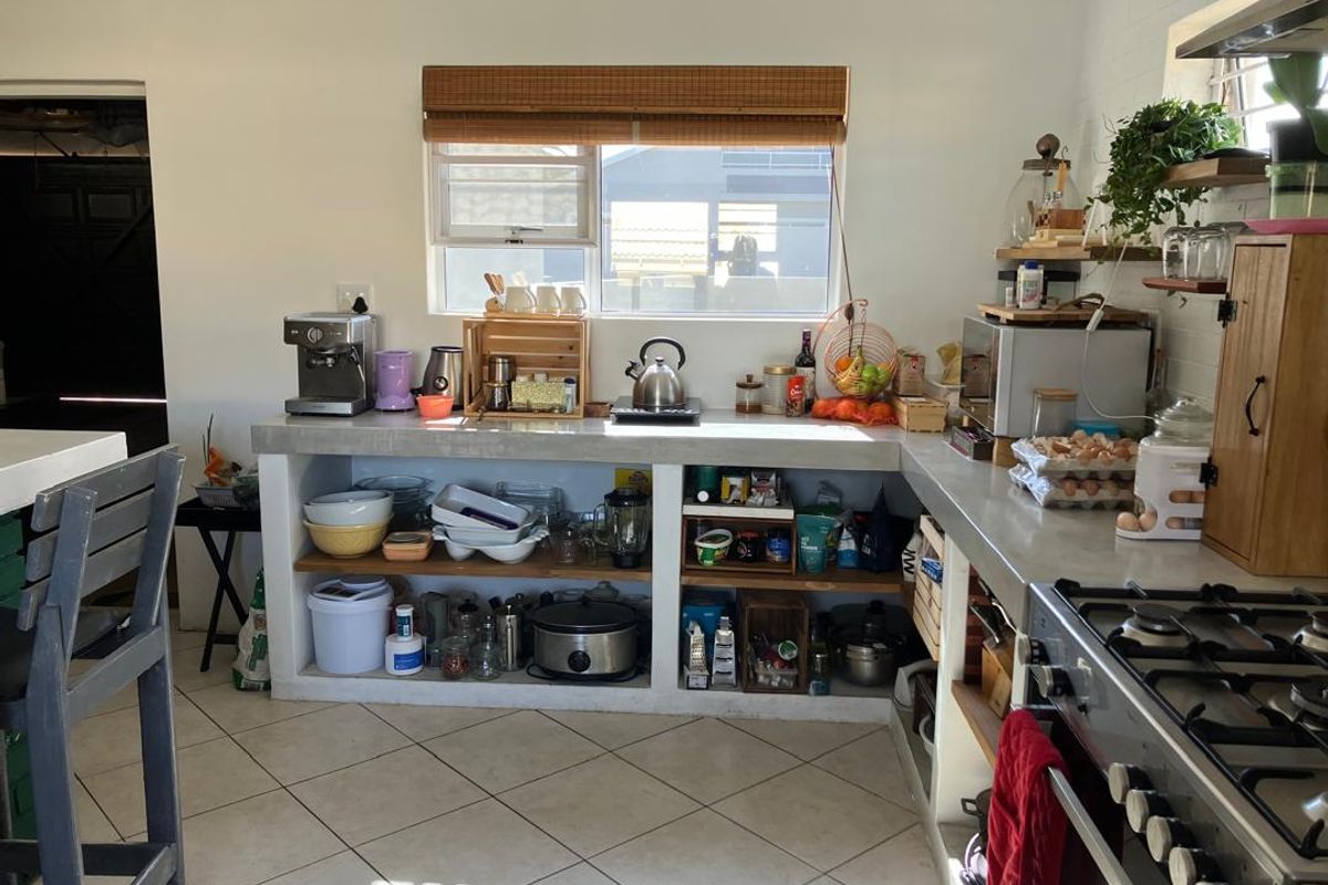 A functional kitchen featuring concrete countertops, open shelving, and a gas stove, with tiled flooring and natural light from a window.