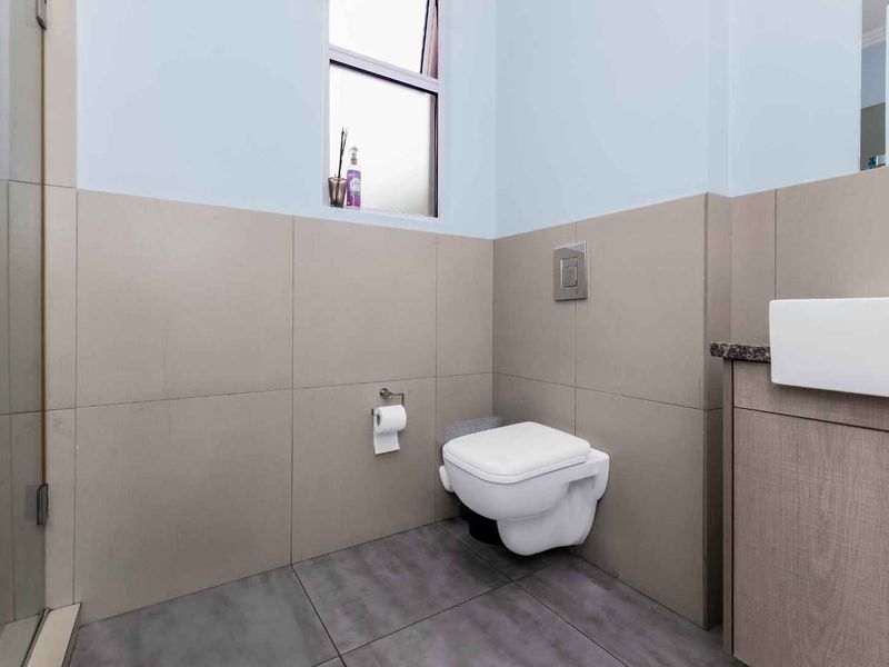 Modern bathroom featuring a wall-mounted toilet, vanity cabinet with a vessel sink, granite countertop, and a glass-enclosed shower with neutral wall and floor tiling.