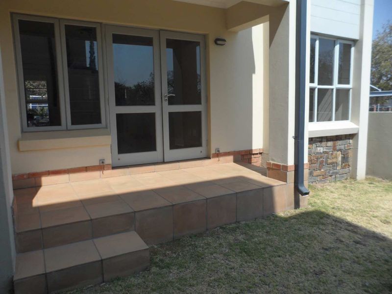 A covered tiled patio area featuring double glass doors, stone cladding accents, and direct access to the garden.