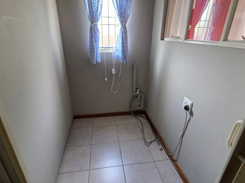 A functional laundry area featuring tiled flooring, dedicated plumbing connections for appliances, and a window with security bars.