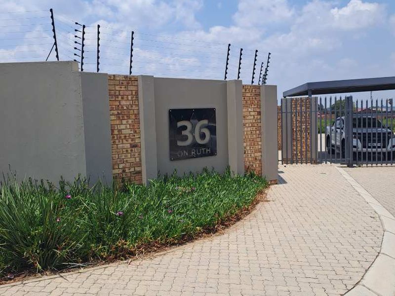 Front entrance view of the residential property featuring a brick boundary wall, electric fencing, and a paved driveway leading to the gate.