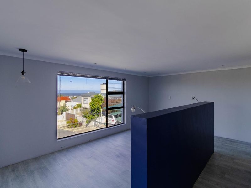 An empty, light-filled living area featuring modern laminate flooring, a central partition wall, and a large window offering neighborhood views.