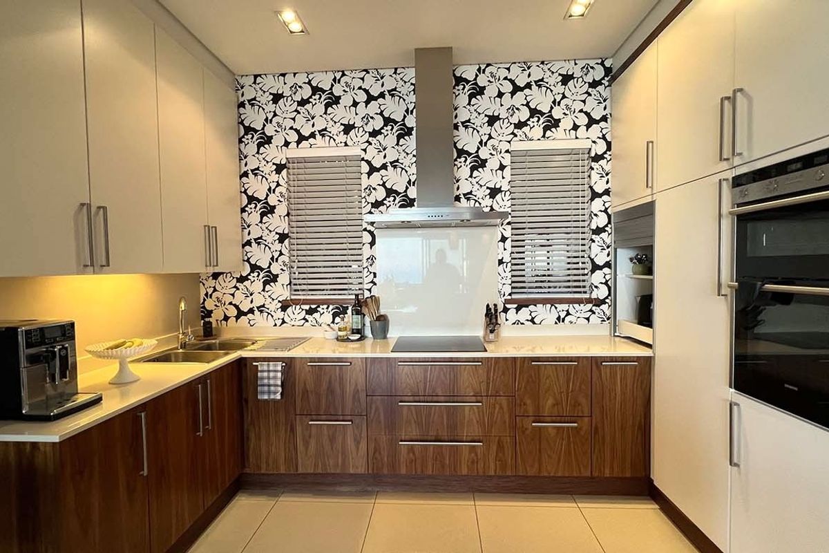 Modern galley-style kitchen featuring two-tone cabinetry, integrated oven, stainless steel extractor fan, and a patterned feature wall with dual windows.
