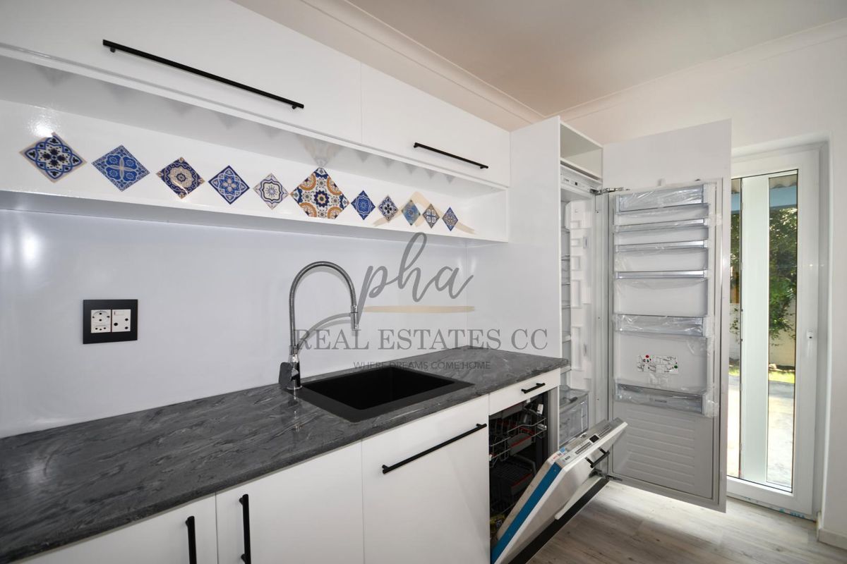 Modern kitchen featuring white cabinetry, dark stone-look countertops, a black undermount sink, integrated dishwasher, and decorative tile backsplash.