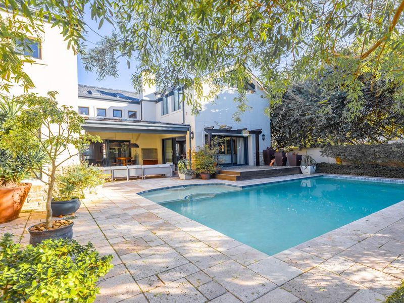 A spacious rear garden featuring a swimming pool, stone-paved patio, and a covered outdoor entertainment area with direct access to the home.
