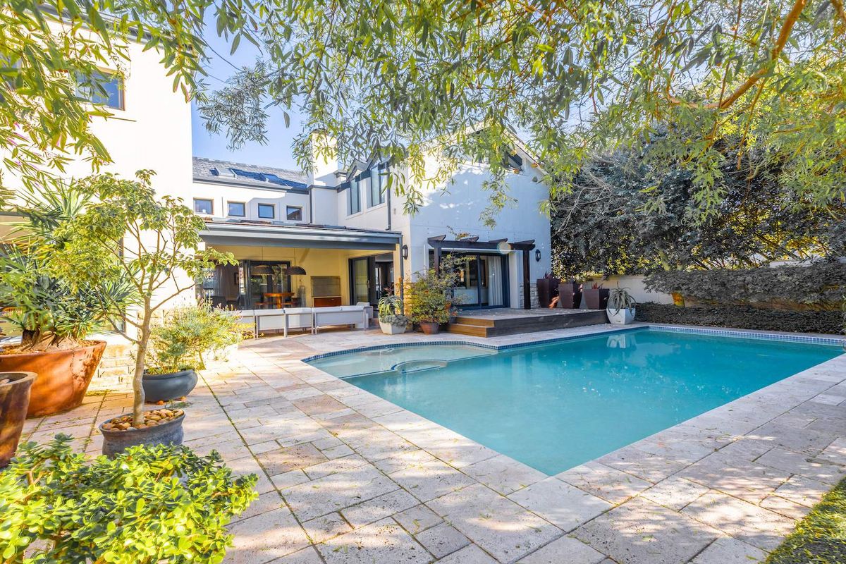 A spacious rear garden featuring a swimming pool, stone-paved patio, and a covered outdoor entertainment area with direct access to the home.