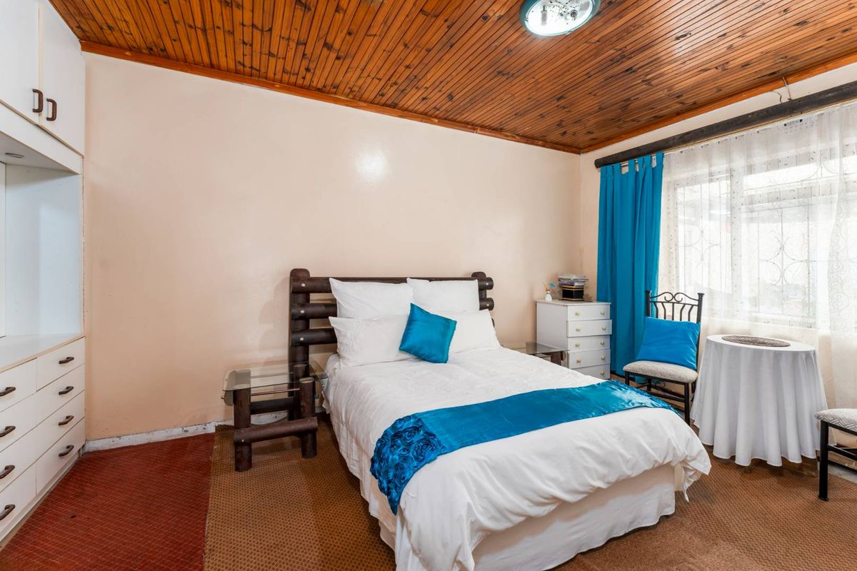 A bedroom featuring a timber-paneled ceiling, built-in cabinetry, and carpeted flooring, offering a functional space with potential for modernization.