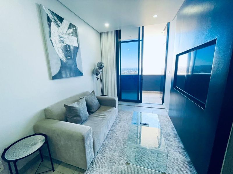 Modern living room featuring a built-in television recess, recessed downlighting, and direct access to a private balcony with expansive views.