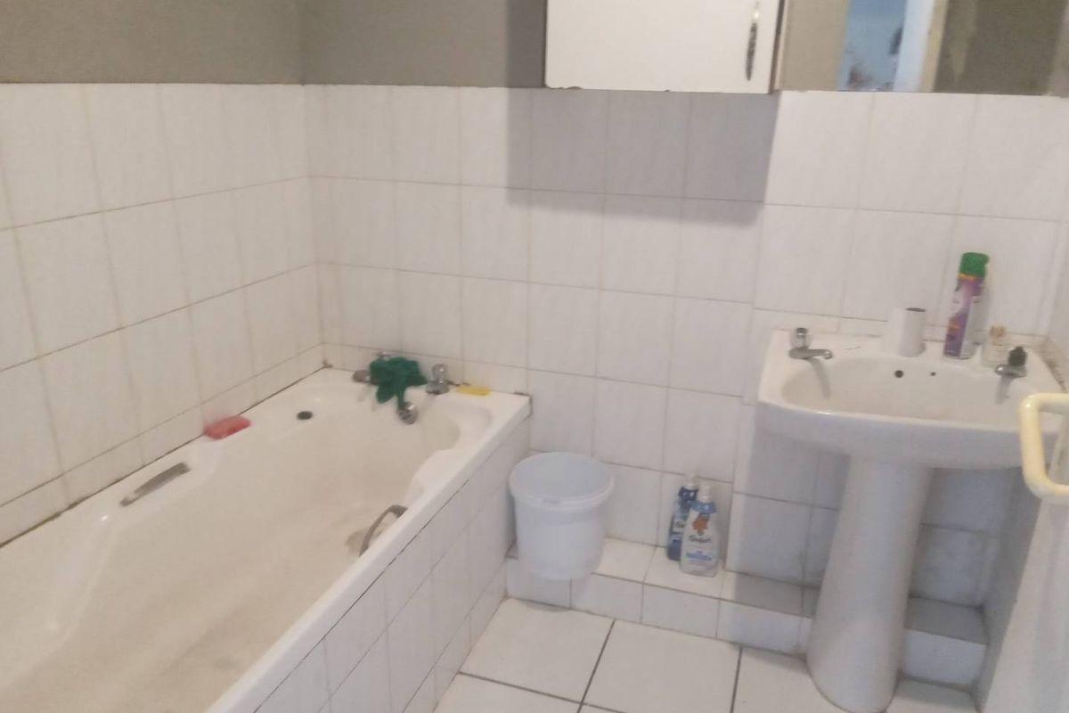 A functional bathroom featuring a standard bathtub, pedestal basin, and wall-mounted cabinet with tiled walls and flooring.