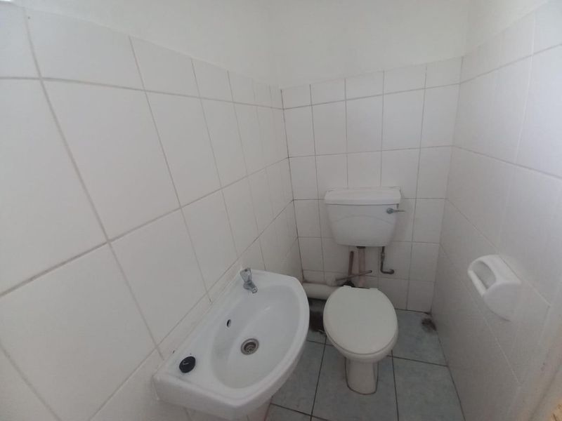 A compact, functional bathroom featuring white wall tiles, a pedestal basin, and a standard toilet with exposed plumbing.