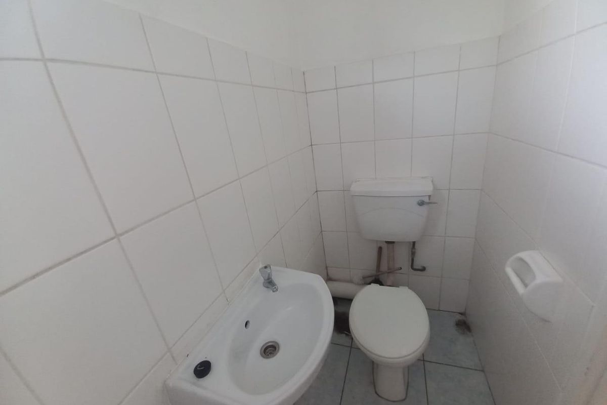 A compact, functional bathroom featuring white wall tiles, a pedestal basin, and a standard toilet with exposed plumbing.