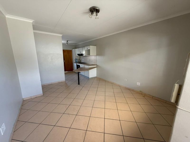 An open-plan living and kitchen area featuring tiled flooring, built-in cabinetry, and a breakfast bar, presenting a blank canvas for potential updates.