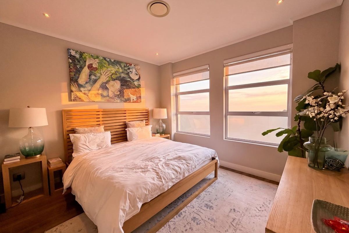A well-lit bedroom featuring large windows with sunset views, recessed ceiling lighting, and neutral wall finishes.