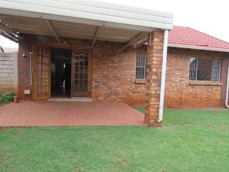A covered brick patio area featuring paved flooring and timber french doors, providing direct access to the rear garden.