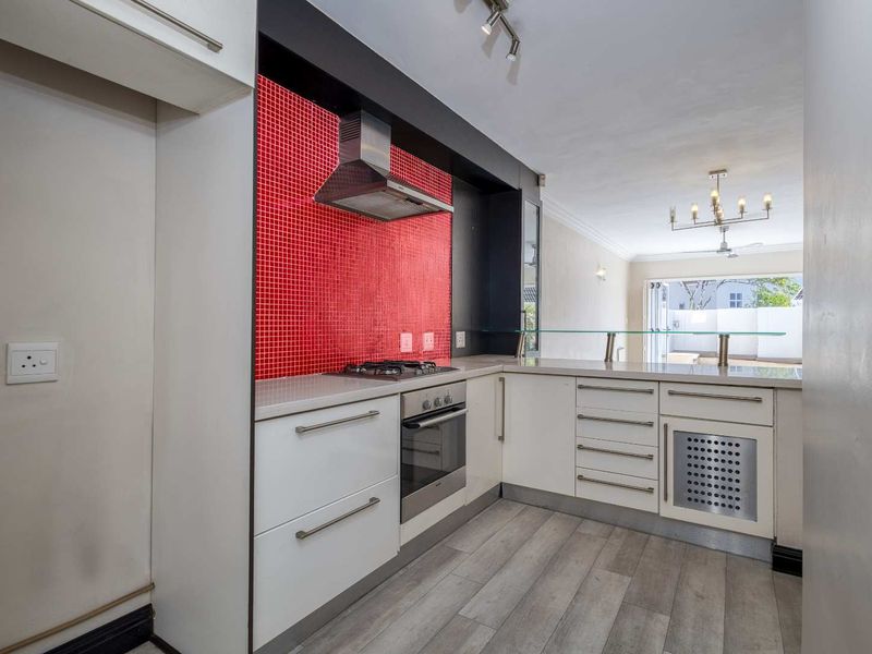 Modern kitchen featuring white cabinetry, stone countertops, a striking red mosaic splashback, built-in oven, gas hob, and an integrated breakfast bar.