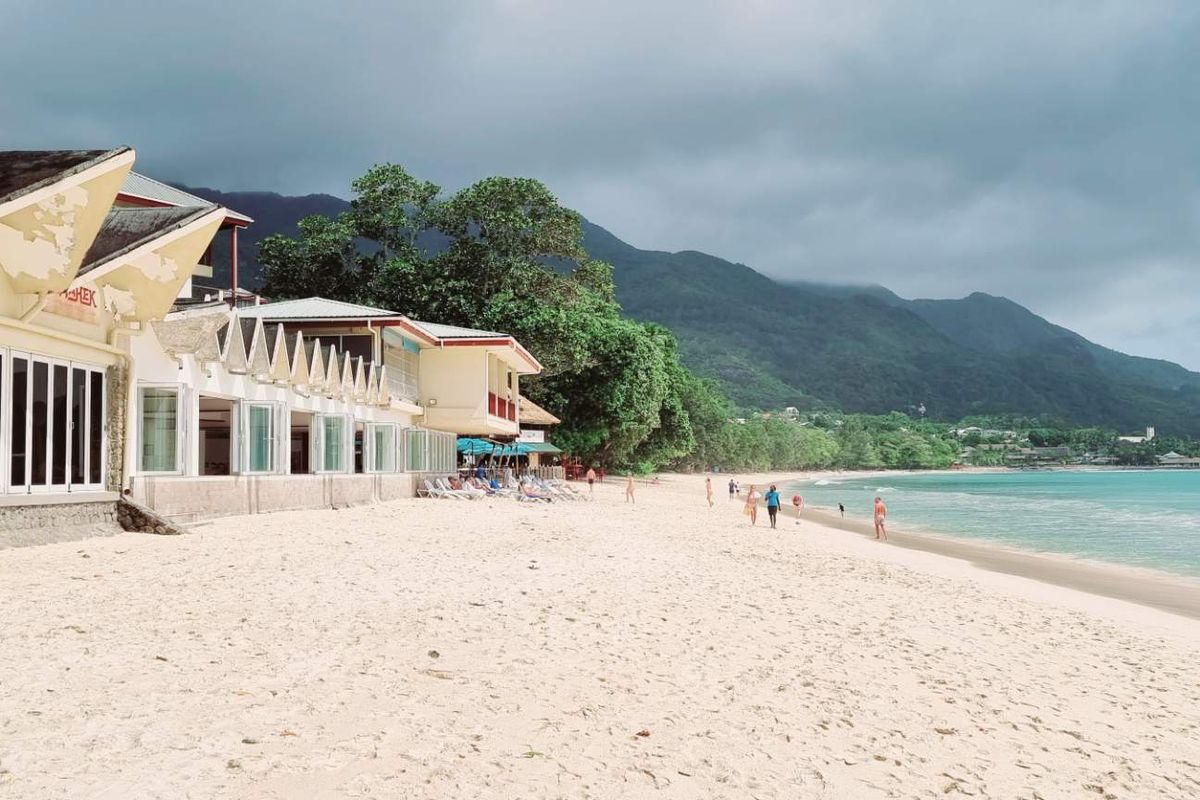 Beachfront view of the villa exterior featuring bi-fold doors and stone masonry, showing signs of weathered paint and exterior wear.