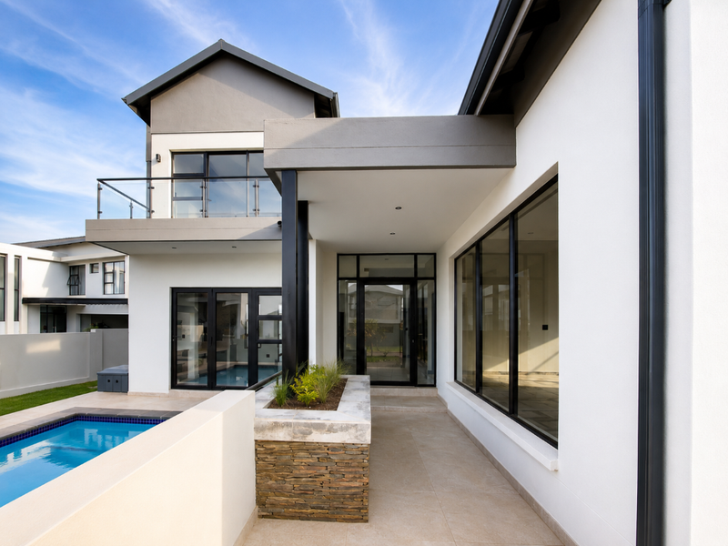 Modern rear exterior featuring a tiled patio, swimming pool, stone-clad planter, and glass balustrade balcony, showcasing contemporary architectural design and clean finishes.