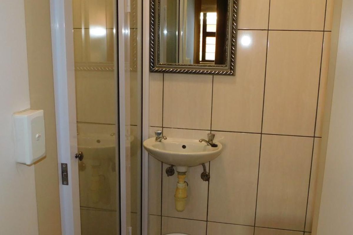 A compact bathroom featuring a wall-mounted basin, toilet, and a shower enclosure with tiled walls.