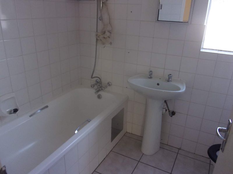 A dated bathroom featuring a standard bathtub, pedestal basin, and tiled finishes, offering a blank canvas for a modern renovation.