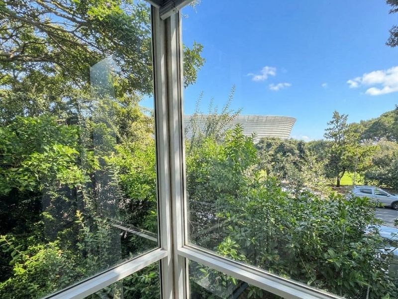 A view from an interior space looking out through large glass windows towards a stadium and surrounding greenery.