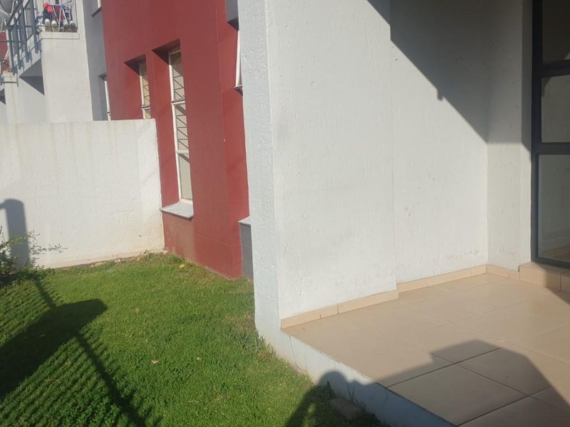 A private rear patio area featuring tiled flooring and direct access to a small garden space through a sliding glass door.