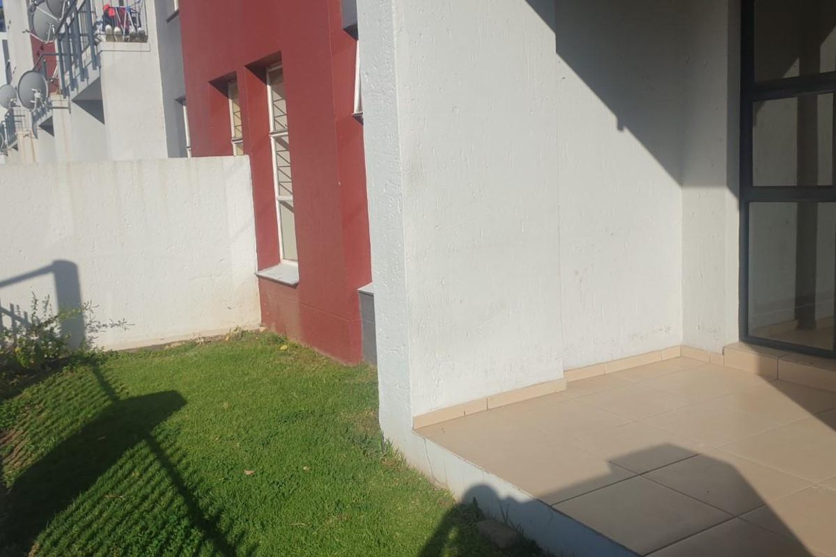 A private rear patio area featuring tiled flooring and direct access to a small garden space through a sliding glass door.