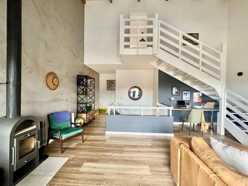 Spacious open-plan living area featuring a wood-burning fireplace, high ceilings, a mezzanine level, and a built-in study nook under the staircase.