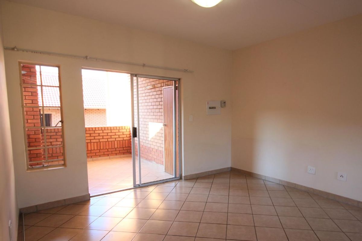 An empty living room featuring tiled flooring, a ceiling light, and a sliding glass door providing access to an outdoor balcony area.
