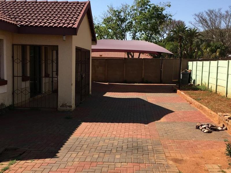 Rear exterior view featuring a paved driveway, perimeter wall, and a shade sail structure providing covered parking space.