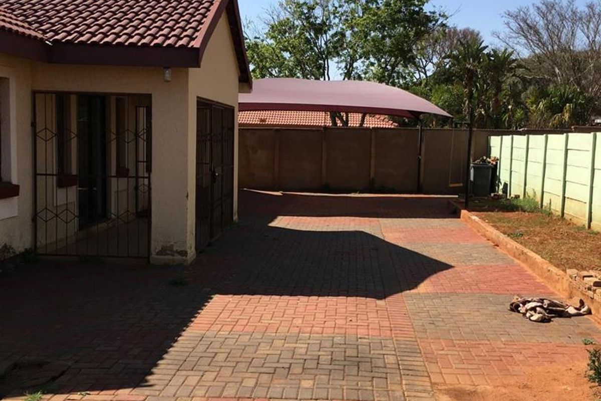 Rear exterior view featuring a paved driveway, perimeter wall, and a shade sail structure providing covered parking space.