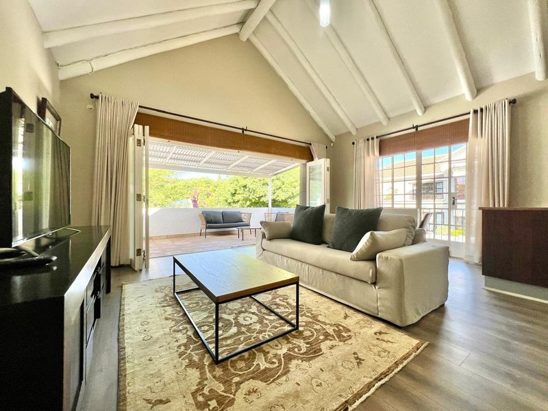 Spacious living room featuring a high vaulted ceiling with exposed rafters, laminate flooring, and large bi-fold doors opening onto a private balcony.