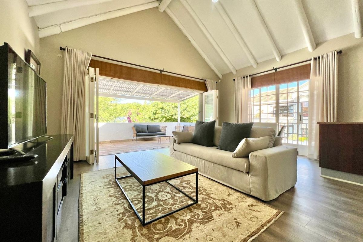 Spacious living room featuring a high vaulted ceiling with exposed rafters, laminate flooring, and large bi-fold doors opening onto a private balcony.
