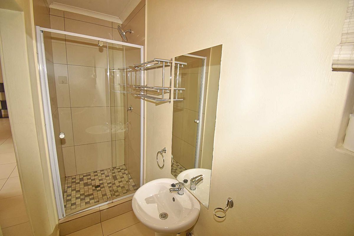 A compact bathroom featuring a glass-enclosed shower with tiled flooring, a wall-mounted basin, and a fitted mirror.