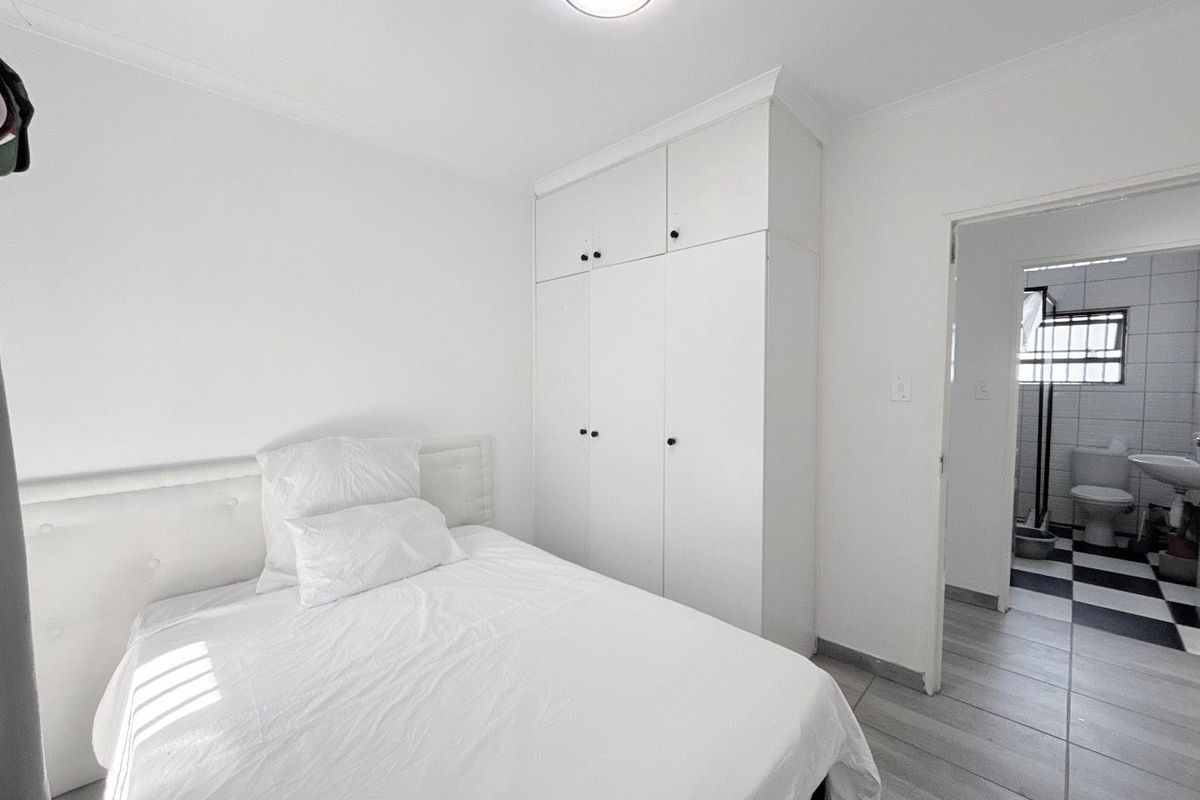 A bright bedroom featuring built-in cupboards and tiled flooring, with an adjoining bathroom visible through the doorway.