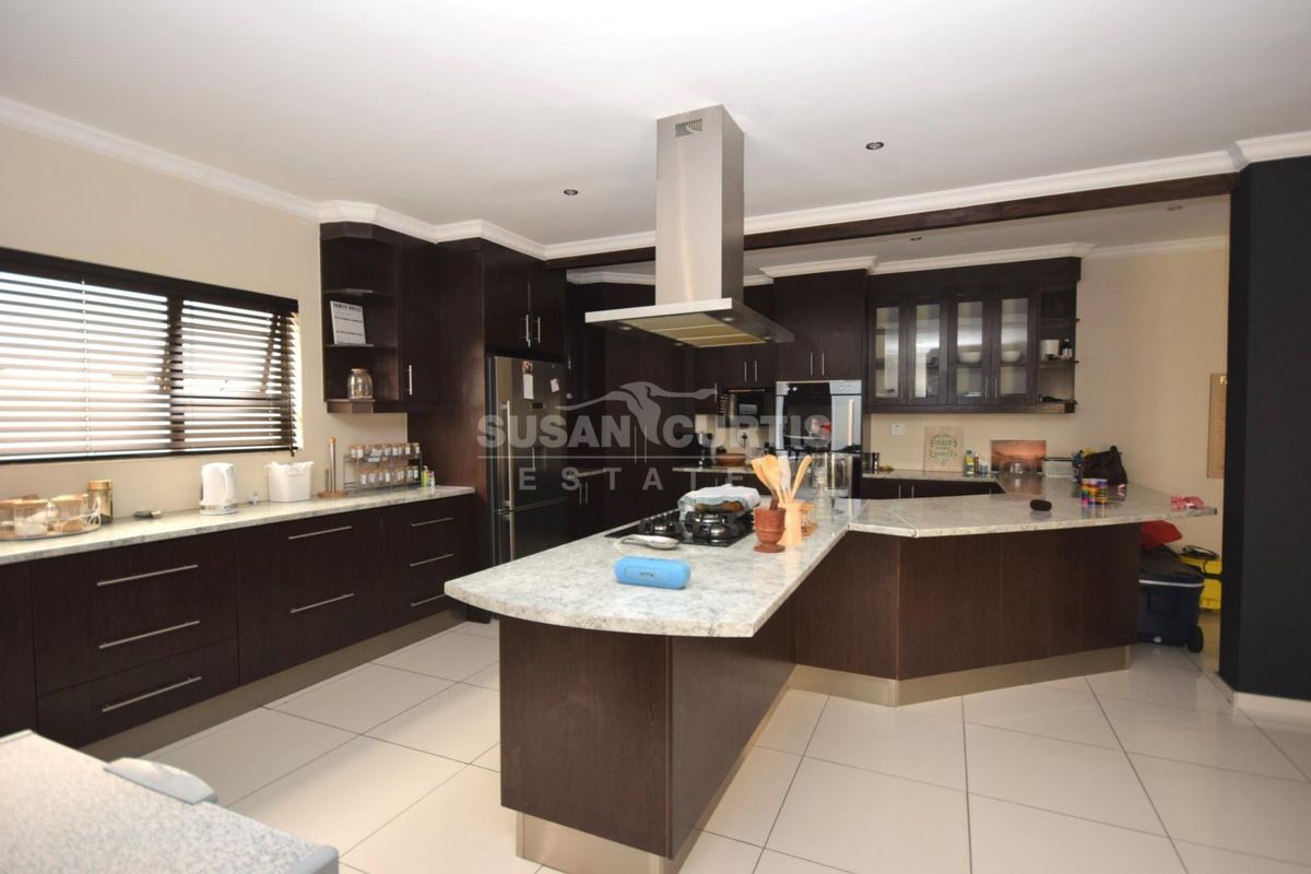 Modern kitchen featuring dark wood cabinetry, stone countertops, a central island with a built-in gas hob, and a stainless steel extractor fan.
