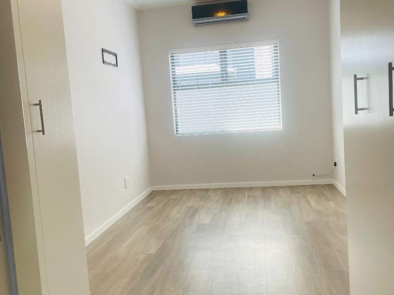 A bright, empty bedroom featuring modern laminate flooring, built-in cupboards, and a wall-mounted air conditioning unit.