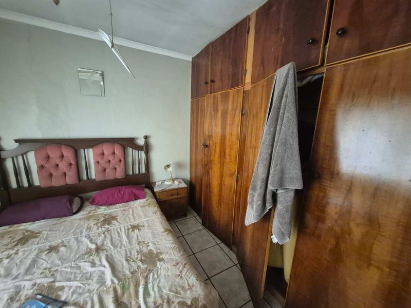 A bedroom featuring built-in wooden cupboards and tiled flooring, currently showing signs of wear and requiring cosmetic updates.