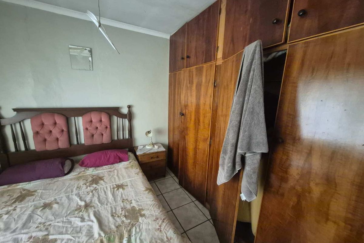 A bedroom featuring built-in wooden cupboards and tiled flooring, currently showing signs of wear and requiring cosmetic updates.