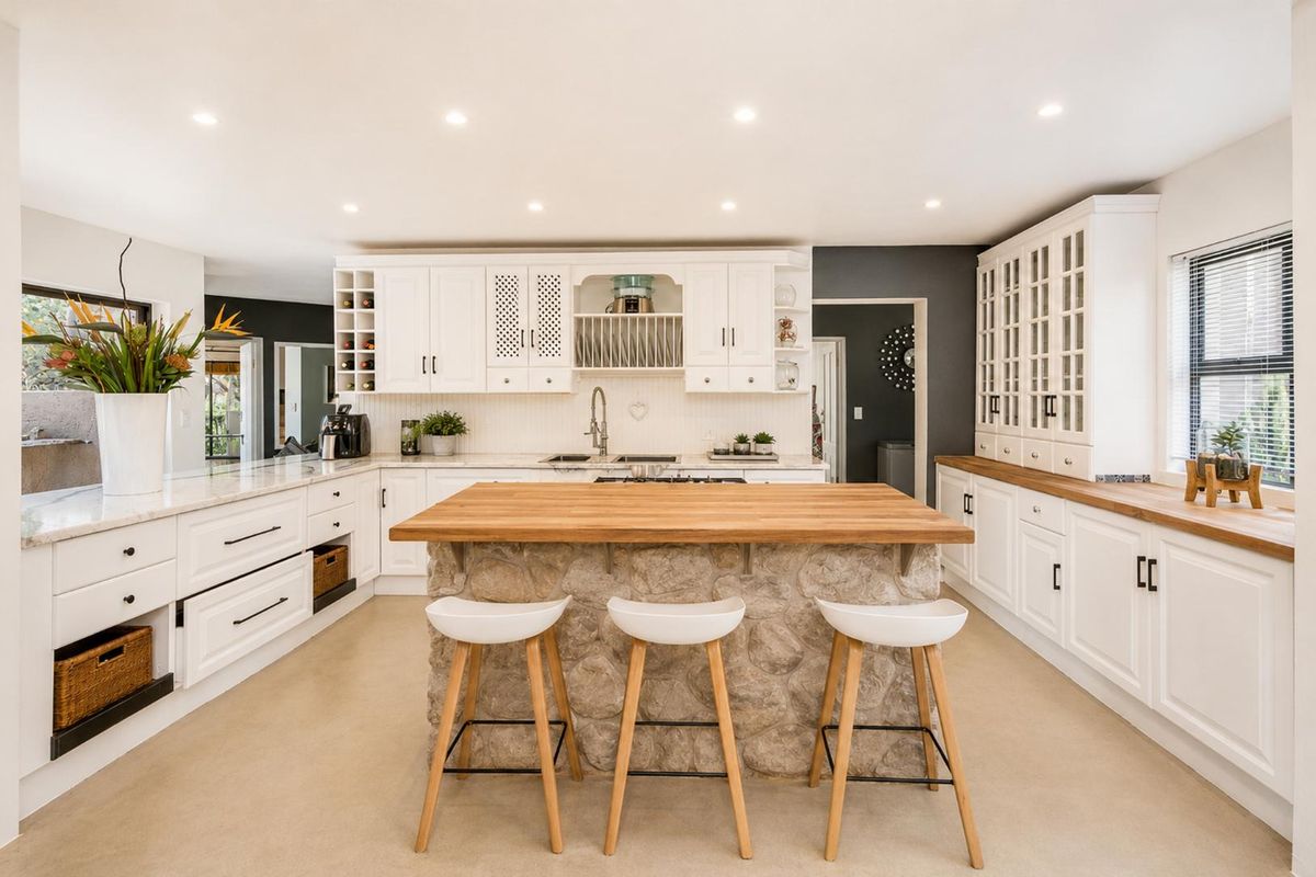A bright, modern kitchen featuring white shaker-style cabinetry, a stone-clad central island with a butcher block top, and high-quality finishes throughout.