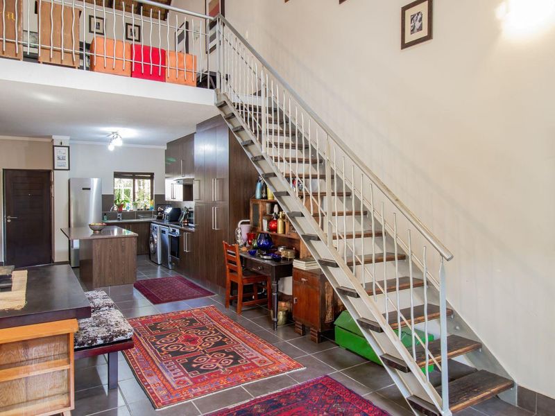 Open-plan living area featuring a modern kitchen with dark cabinetry, tiled flooring, and a prominent staircase leading to an upper mezzanine level.