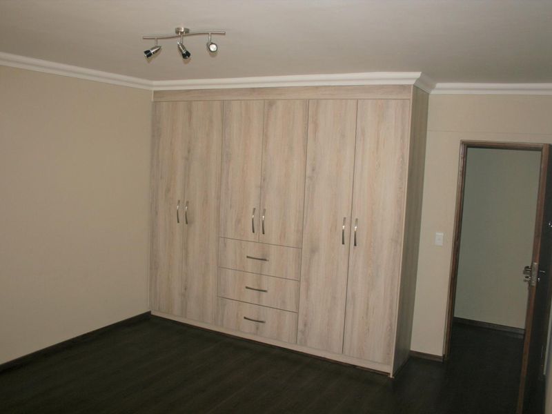 A clean, empty bedroom featuring modern light wood-grain built-in cupboards, dark laminate flooring, and decorative ceiling coving.
