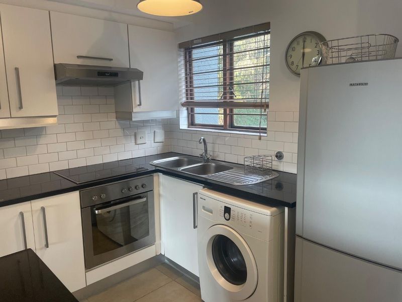 A functional kitchen featuring white cabinetry, subway tile backsplash, dark countertops, and integrated appliances including an oven, hob, and extractor fan.